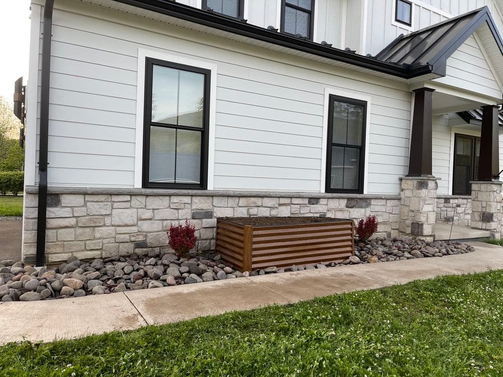 Wooden planter box surrounded by rocks and landscaping at a modern home's exterior.
